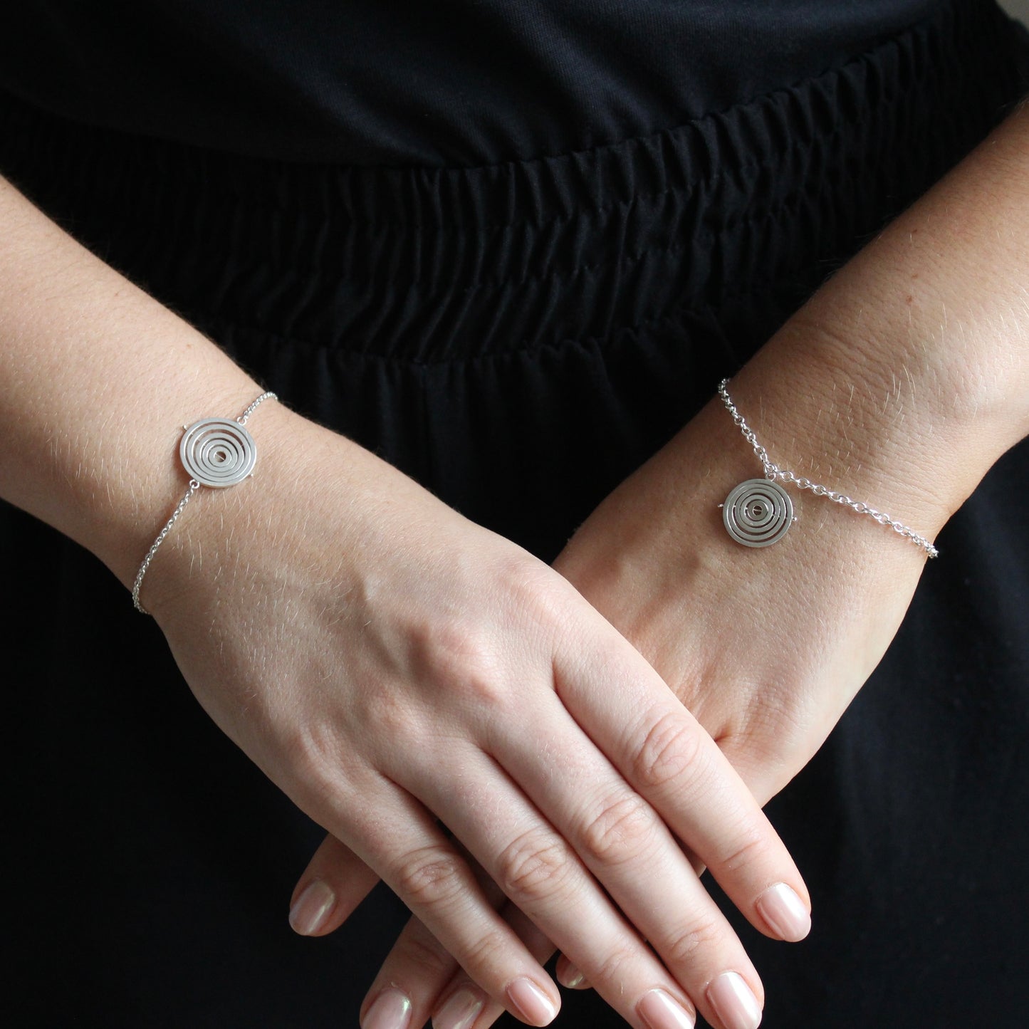 Model wearing 2 styles of sterling silver kinetic bracelets with dainty trace chain and concentric rings held by central pin