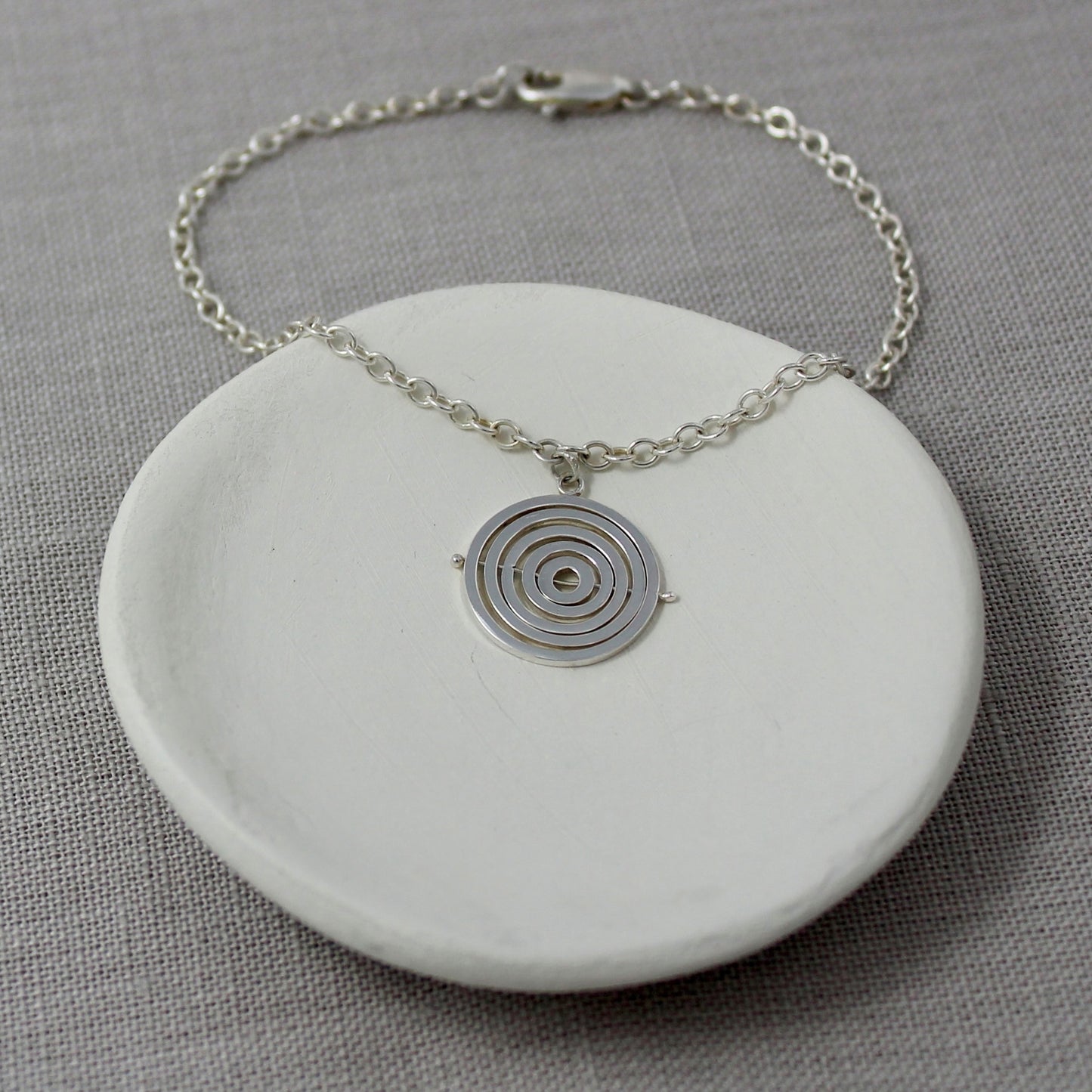 Handcrafted sterling silver kinetic bracelet with concentric circle charm hanging from delicate trace chain and lobster clasp
