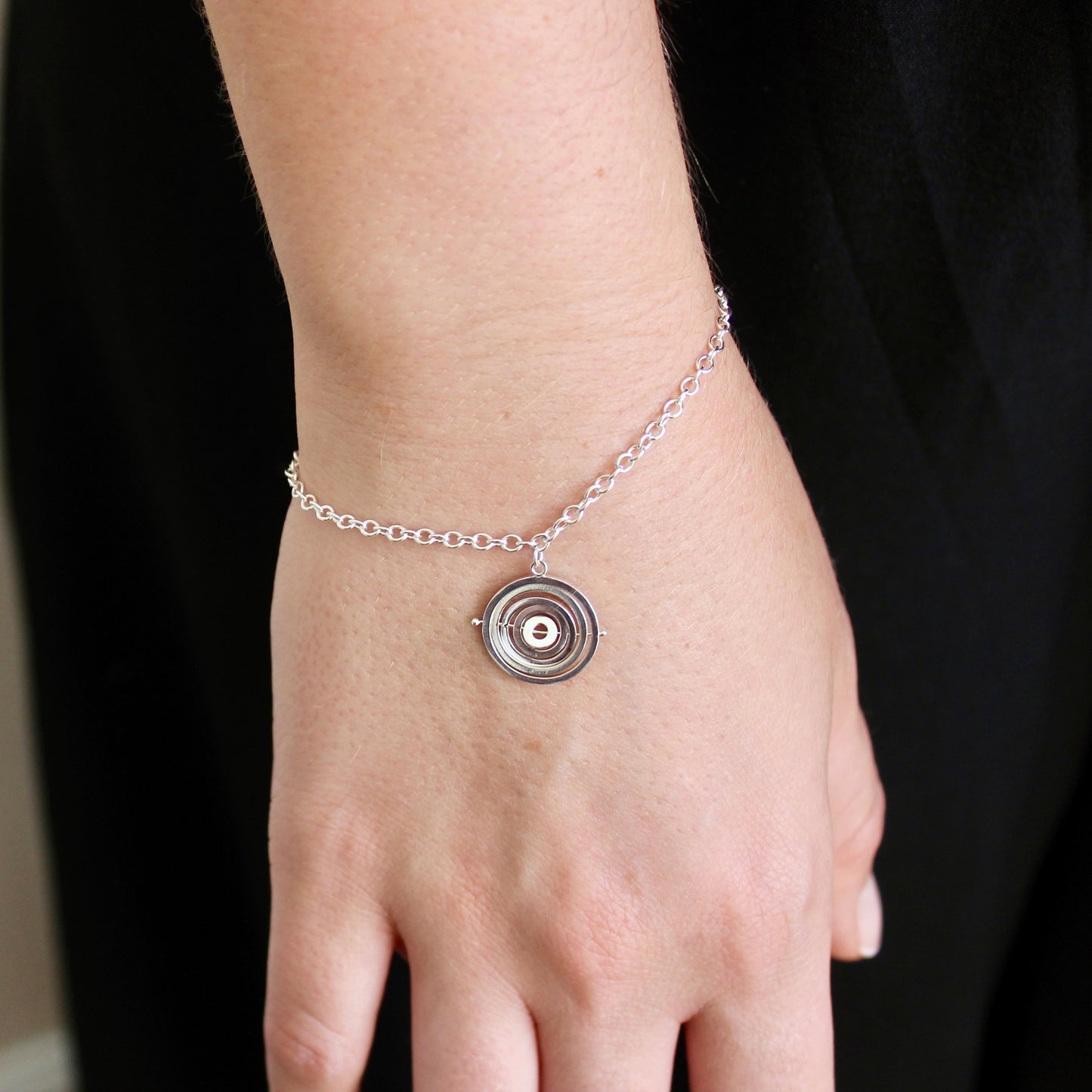 Model wearing dainty sterling silver trace chain bracelet with handmade kinetic concentric circles charm dangling from chain