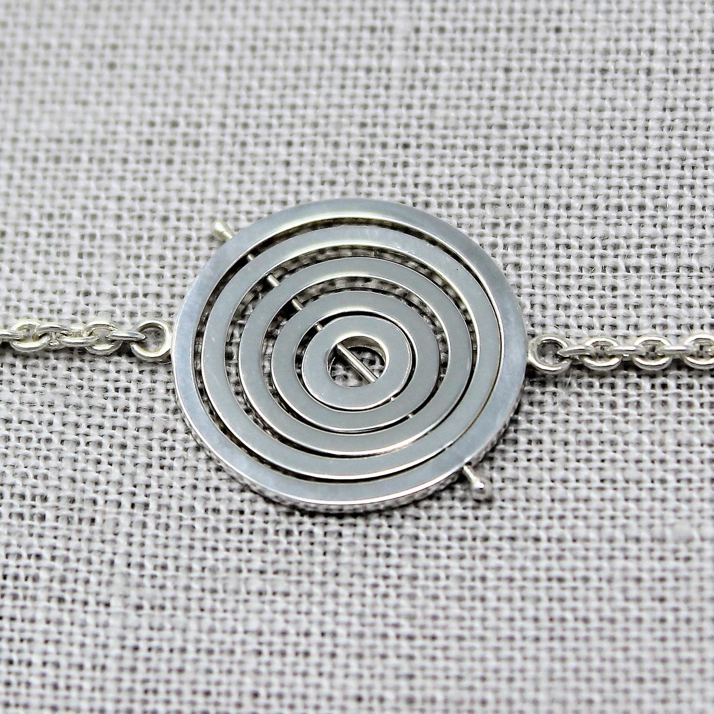 Sterling silver kinetic choker with 5 concentric recycled square wire rings on central pin, attached to trace chain on sides