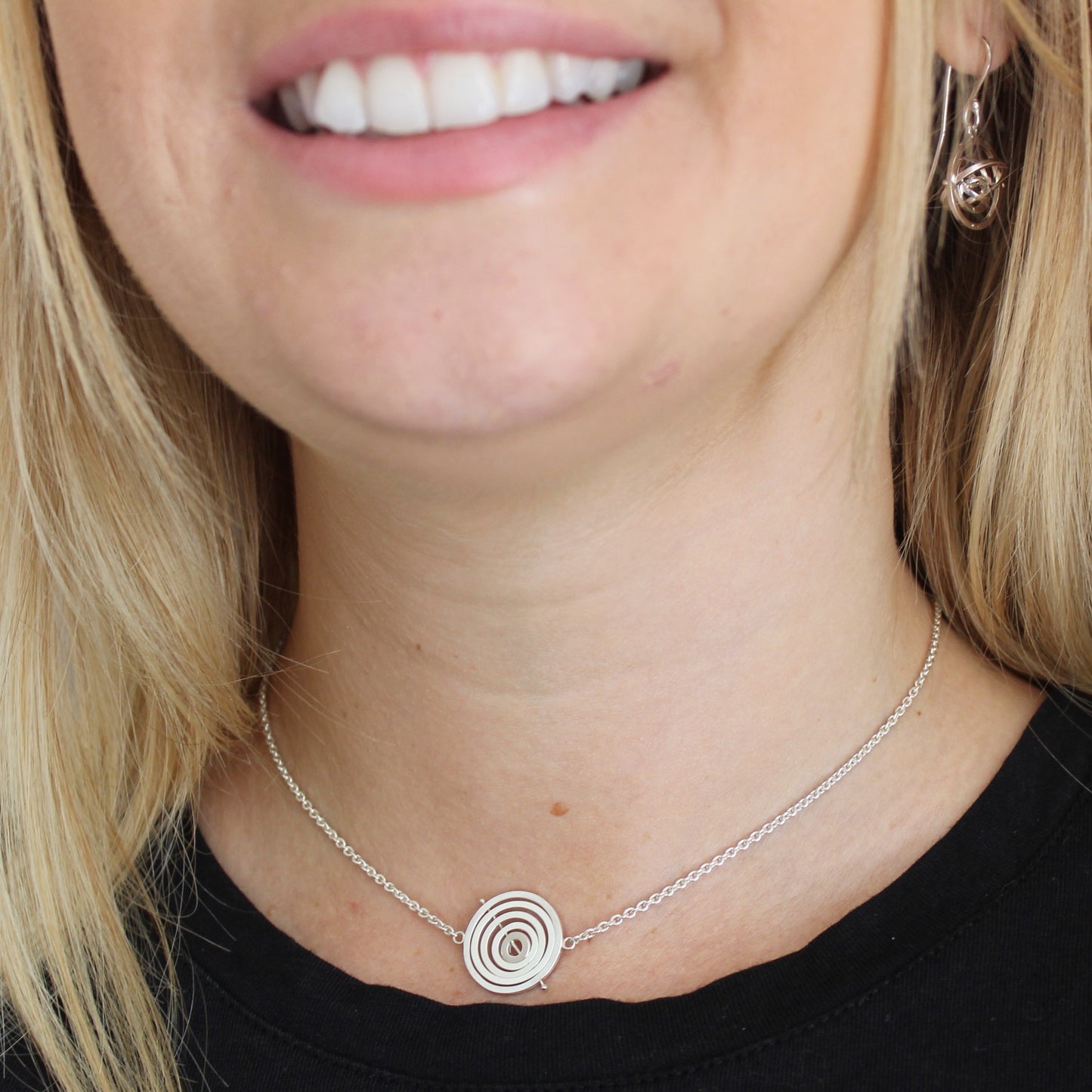 Model wearing handmade silver 1.7cm wide kinetic choker on trace chain hanging at base of throat and matching dangly earrings