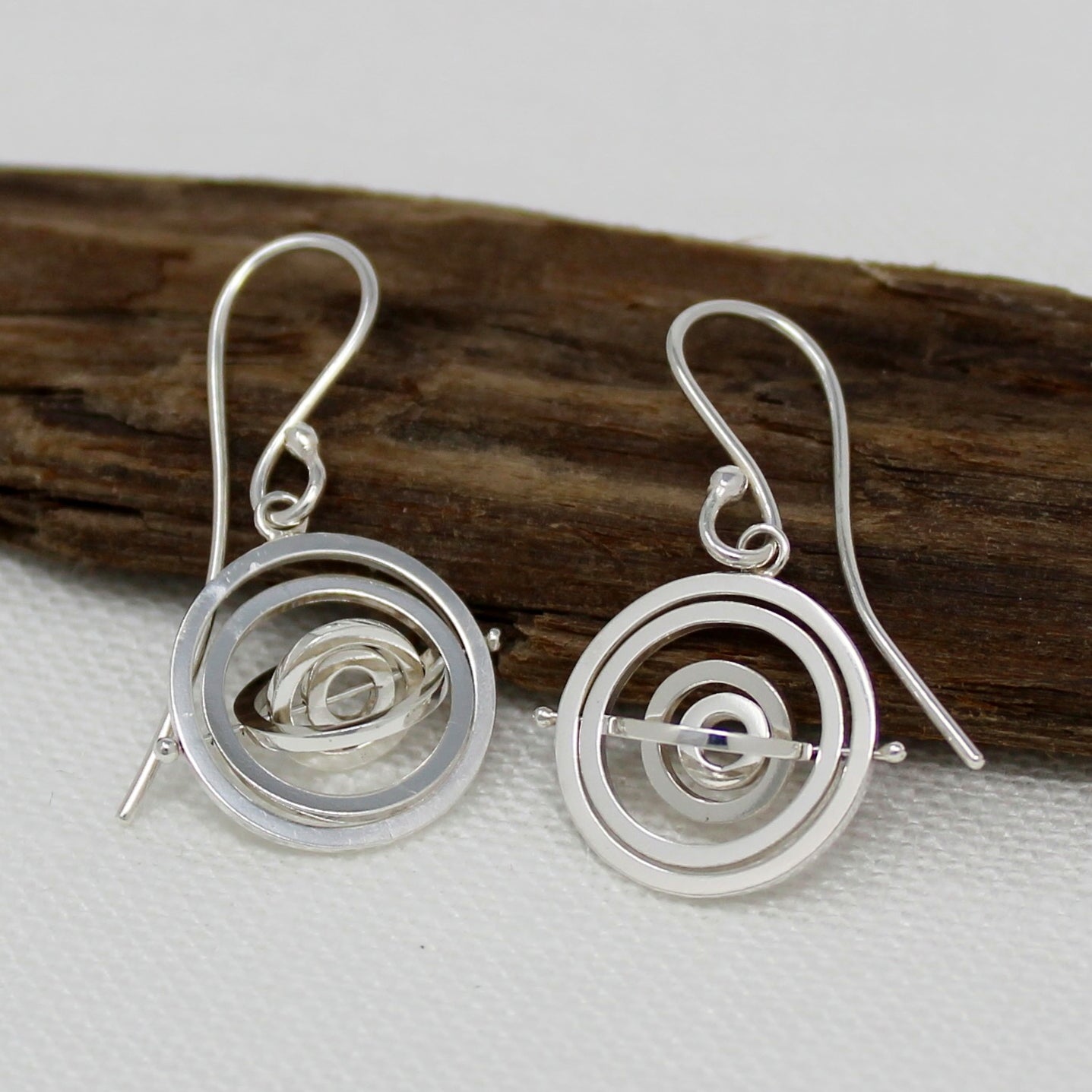 Handcrafted kinetic silver dangly earrings made of 5 intricate concentric rings pivoting around a central pin on earwire hook