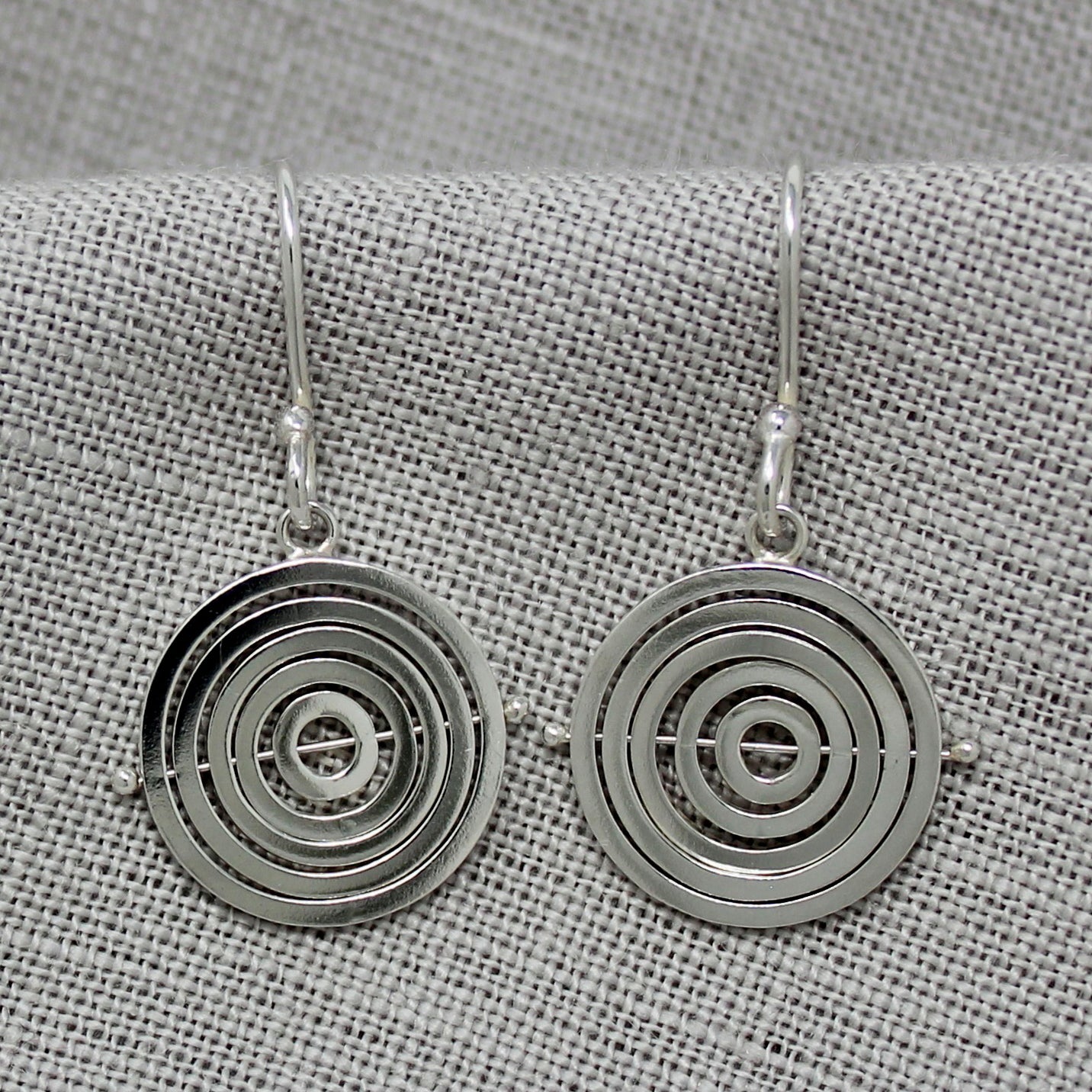 Sterling silver kinetic dangly earrings with 5 concentric recycled square wire rings on central pin, attached to hook earwire