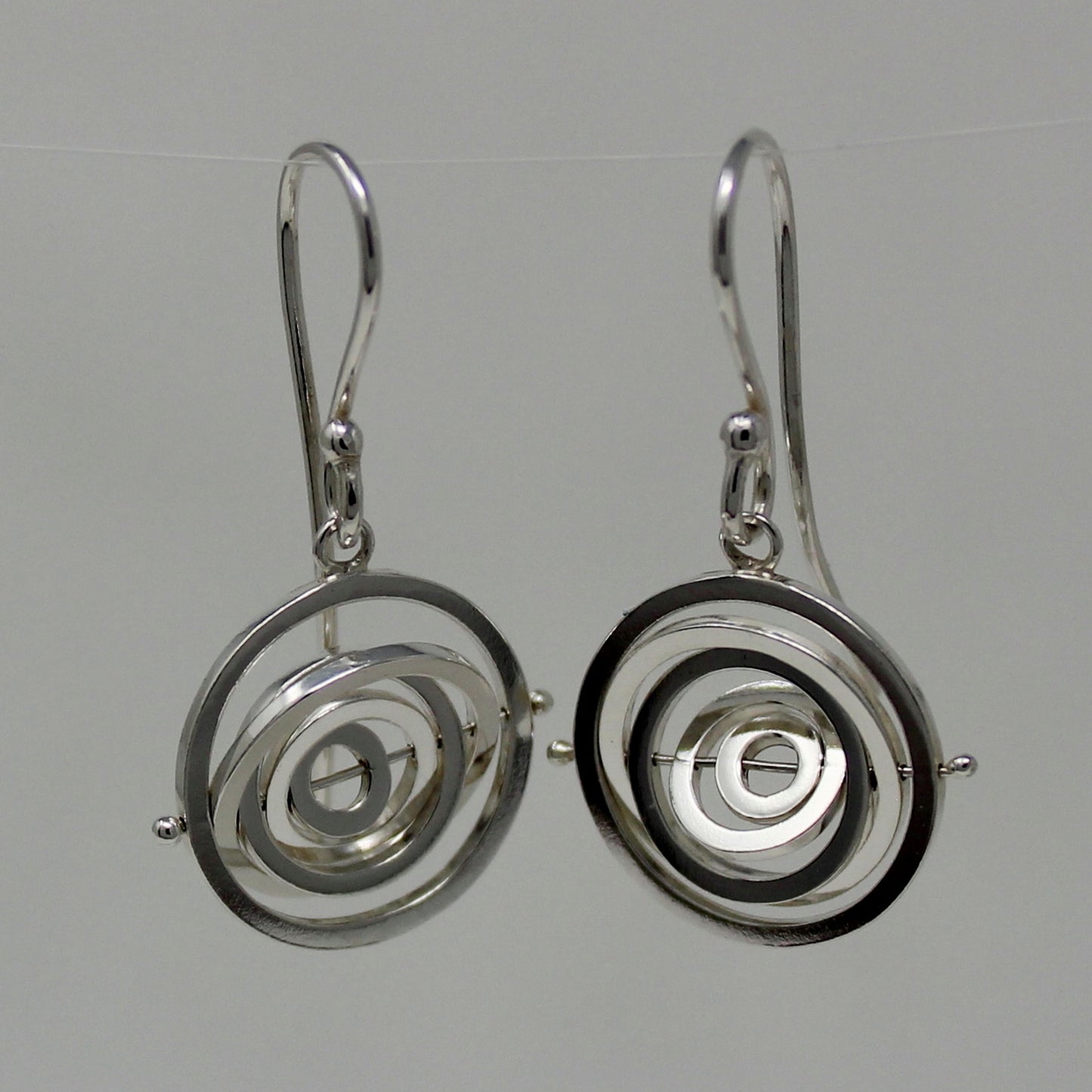 Delicate silver kinetic dangly earrings 1.4cm wide with 5 concentric rings spinning on central pin hanging from earwire hook