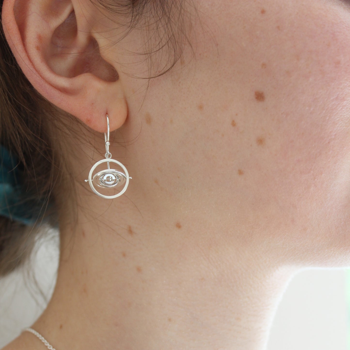 Model wearing dainty handmade kinetic silver earrings with earwire hook and 5 spinning concentric wire rings with 2.9cm drop