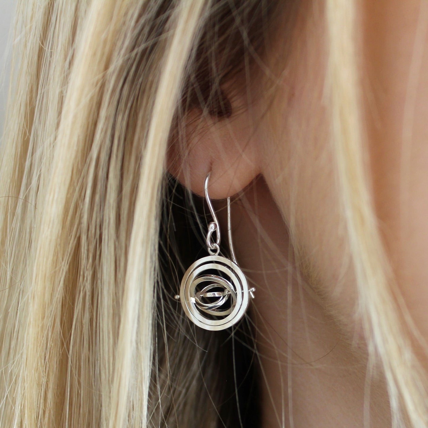 Model wearing kinetic silver dangly earrings with earwire & 5 concentric wire rings pivoting on a central pin with 2.9cm drop