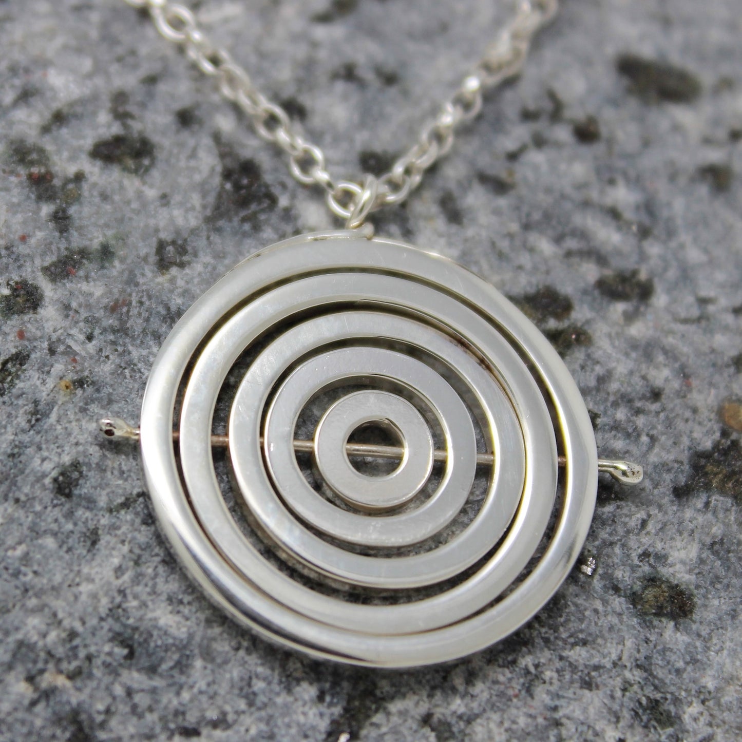Sterling silver 2.2cm wide kinetic necklace with 5 concentric recycled square wire rings held by central pin, on belcher chain