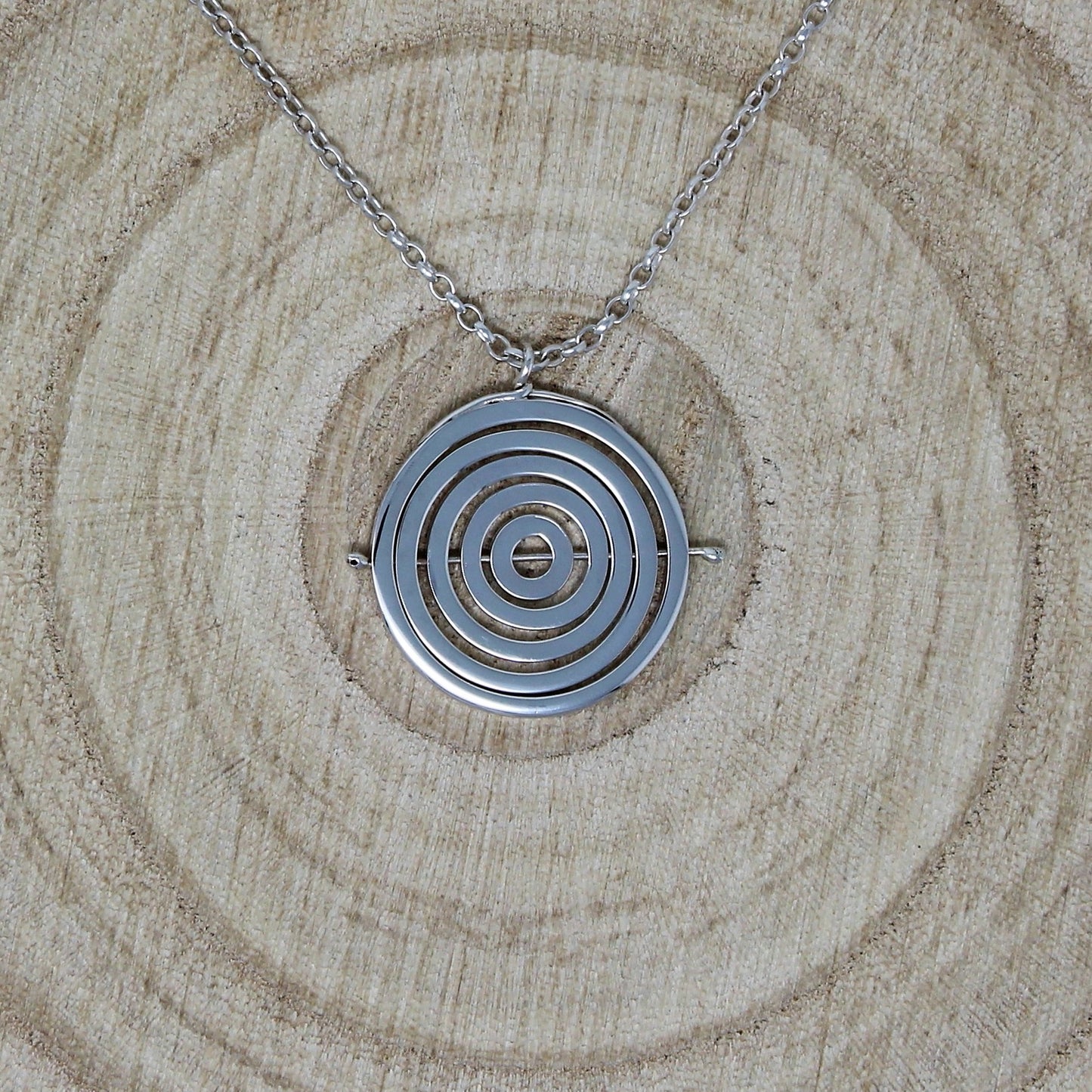 Handmade sterling silver kinetic necklace with 5 concentric circle recycled wire rings held by central pin, on belcher chain