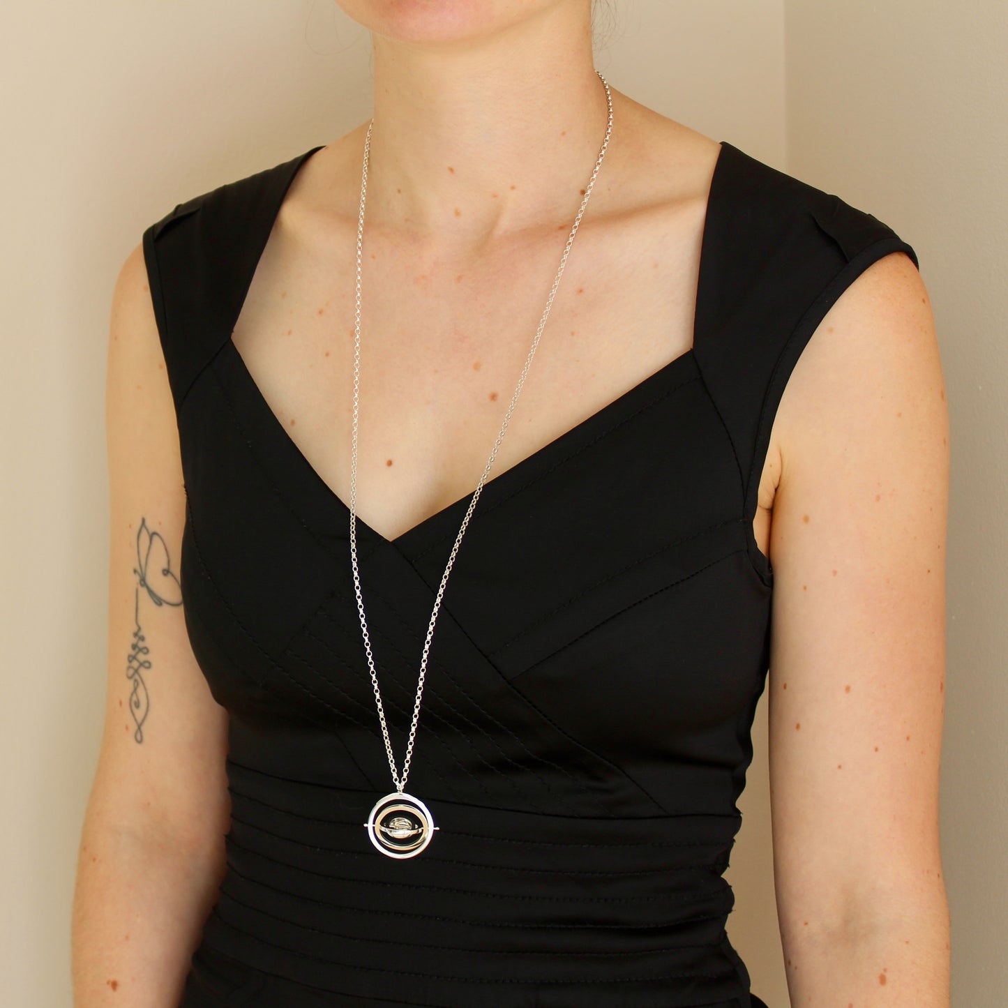 Model wearing hallmarked silver 3cm wide Concentric Circle kinetic pendant on 80cm chunky belcher chain hanging below bustline