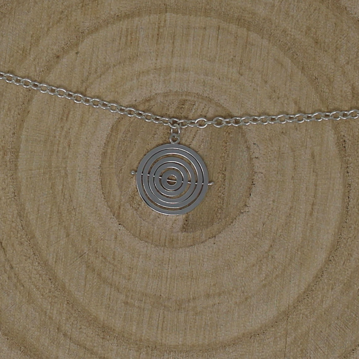 Handcrafted sterling silver kinetic charm bracelet with 5 concentric recycled wire rings held by central pin, on trace chain