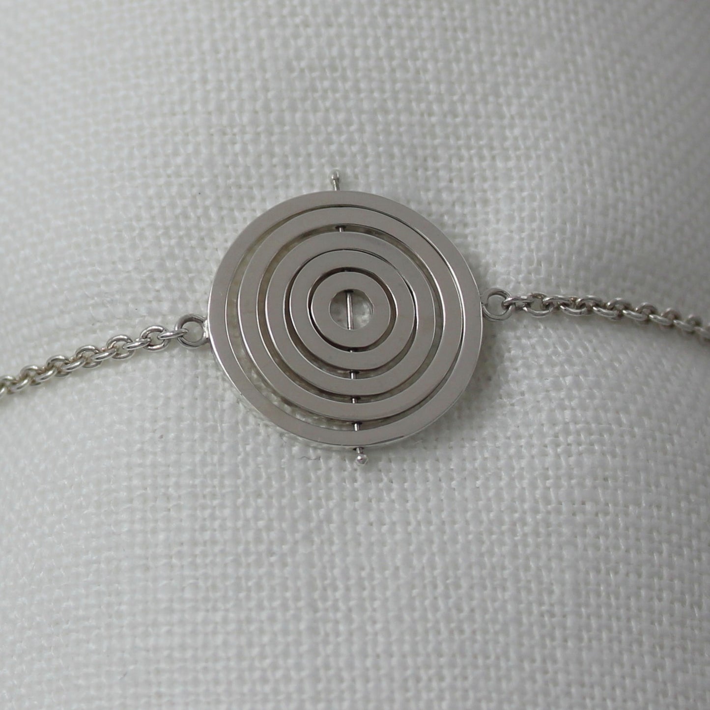 Sterling silver kinetic bracelet with 5 concentric recycled square wire rings on central pin attached to trace chain on sides