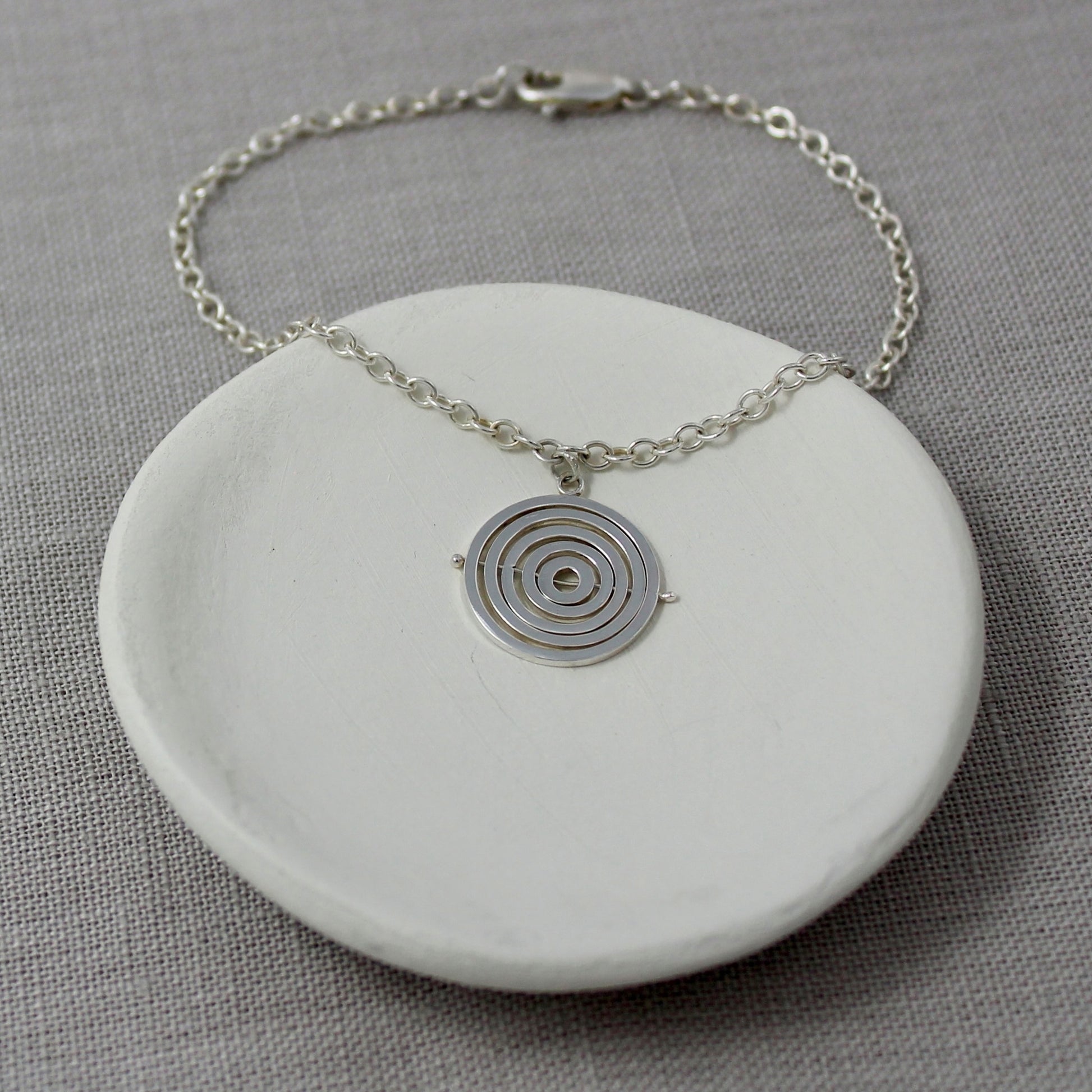 Handcrafted sterling silver kinetic bracelet with concentric circle charm hanging from delicate trace chain and lobster clasp