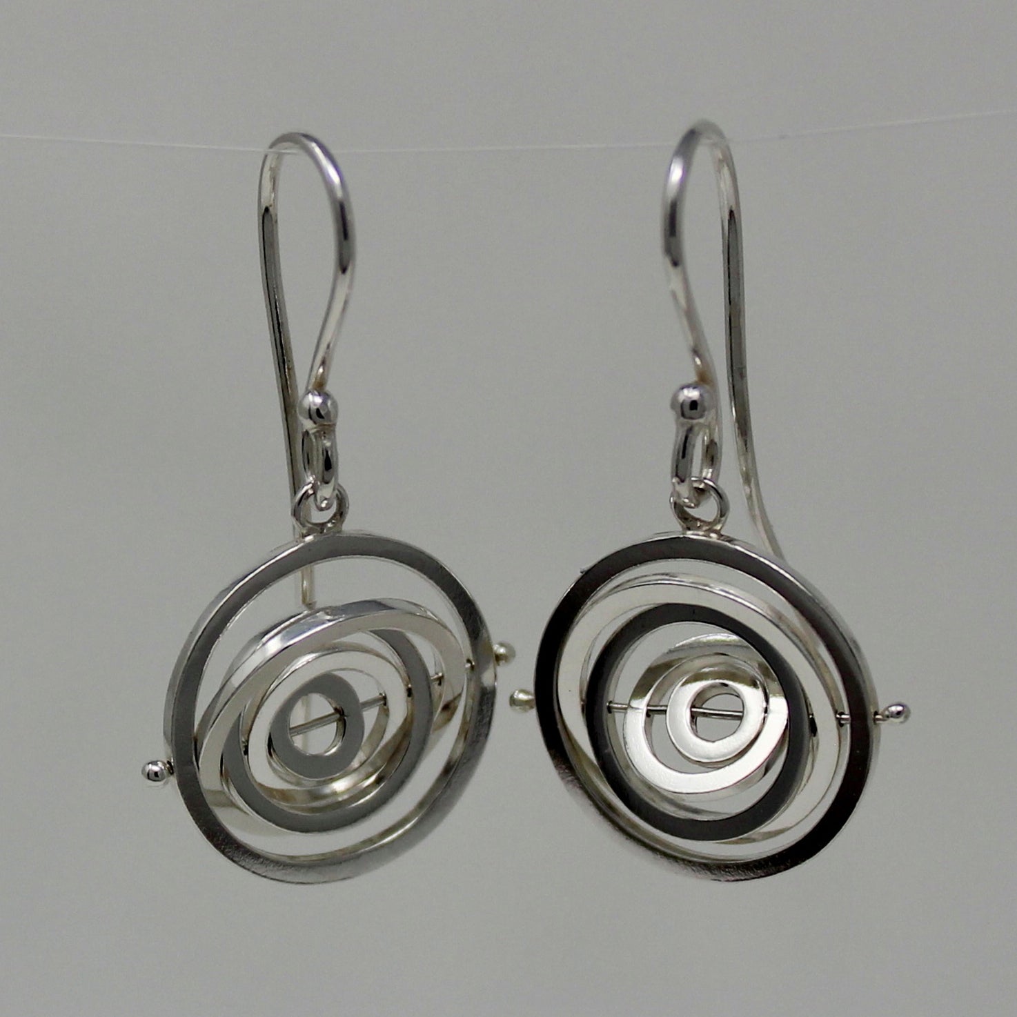 Delicate silver kinetic dangly earrings 1.4cm wide with 5 concentric rings spinning on central pin hanging from earwire hook